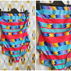 Puede incluir: Un traje de baño sin tirantes con un estampado geométrico colorido en tonos rojos, azules, amarillos y morados. El estampado presenta rayas y zigzags.