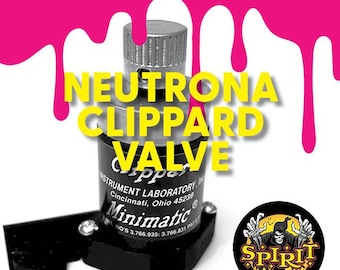 May include: A black Clippard Minimatic valve with the text "NEUTRONA CLIPPARD VALVE" in yellow letters. The valve is labeled "INSTRUMENT LABORATORY, INC. Cincinnati, Ohio 45239" and has the text "Minimatic" in a circle with the text "NO'S 3.766.935: 3.766.831 PAT'S" below it. The valve is sitting on a pink surface.