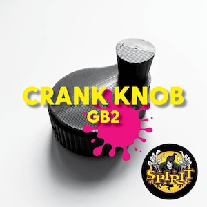 May include: A black 3D printed crank knob with the text "GB2" printed on it. The knob is on a white surface with a pink splatter paint design.