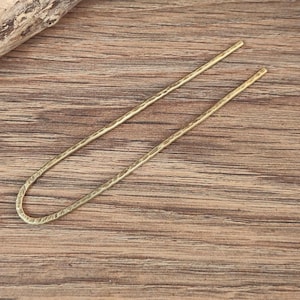 May include: A gold metal hair stick with a textured surface.