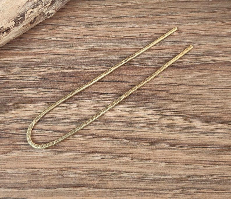 May include: A gold metal hair stick with a textured surface.