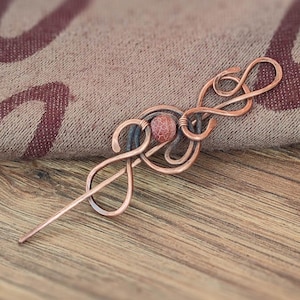 May include: A copper wire hair stick with a red stone accent, shaped like a treble clef.