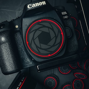 Op de afbeelding: Een zwarte Canon EOS 90D camera met een rode en zwarte lensdop. De camera wordt omringd door verschillende zwarte en rode lensdoppen.