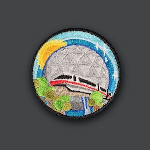 May include: Embroidered patch depicting the Spaceship Earth attraction at Epcot, with a monorail train passing in front of it. The patch features a blue sky, white stars, and green trees.