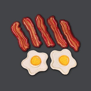 Può includere: Sei toppe di feltro ricamate a forma di strisce di pancetta e uova al tegamino. La pancetta è rossa e le uova sono gialle con contorni bianchi.