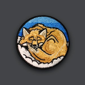 Pode incluir: Etiqueta bordada de uma raposa enroscada dormindo em uma nuvem branca com um fundo de céu azul.