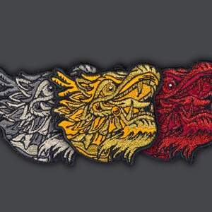 May include: Three embroidered iron-on patches featuring dragon heads in different colors: gray, yellow, and red.