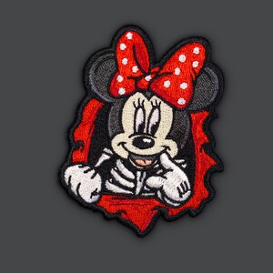 Könnte beinhalten: Ein gestickter Aufnäher mit einer Comic-Maus mit einer roten Schleife mit weißen Punkten. Die Maus schaut aus einem roten und schwarzen zerrissenen Loch.