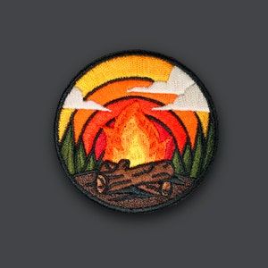 May include: Embroidered patch with a campfire scene. The patch features a sunset with orange, yellow, and red hues, a campfire with flames, and green trees.