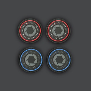 Op de afbeelding: Vier zwarte ronde patches met een kompasontwerp en een camera lens in het midden. Twee patches hebben een rode rand en twee patches hebben een blauwe rand.