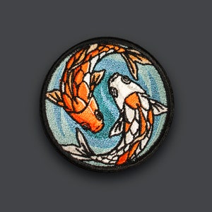 Pode incluir: Etiqueta bordada com dois peixes koi nadando em círculo. Os peixes são laranja e branco com contornos pretos. O fundo é azul com redemoinhos brancos.
