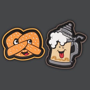 May include: Two cartoon patches, one of a pretzel and one of a beer stein. The pretzel is orange and brown with a smiling face and the beer stein is gray with a white foam top and a smiling face with a red tongue sticking out.