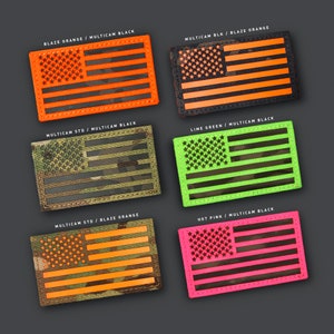 Può includere: Toppe rettangolari con un design a bandiera americana in varie combinazioni di colori. Le toppe includono arancione acceso, nero, verde lime e rosa acceso, con etichette di testo come "BLAZE ORANGE / MULTICAM BLACK".