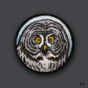 May include: A round embroidered patch featuring a detailed gray owl with yellow eyes. The owl's face is centered in the patch, with its feathers and beak visible.