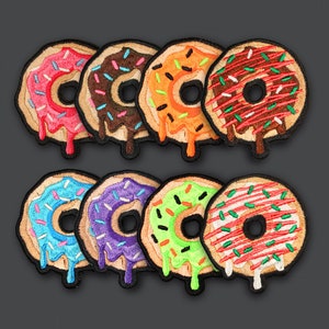 Pode incluir: Oito patches bordados de donut em várias cores, incluindo azul, verde, roxo, laranja, vermelho e marrom. Cada donut tem granulado branco e um glacê branco.
