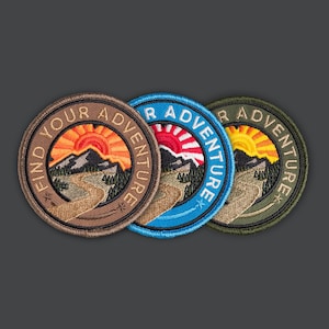 May include: Three round embroidered patches with a mountain and sun design. The patches are brown, blue, and green, each with the words "Find Your Adventure" or "Your Adventure" in a circular pattern.