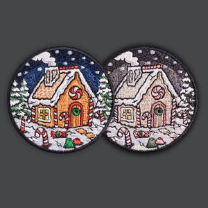 Op de afbeelding: Twee ronde geborduurde patches met een peperkoekhuisontwerp. De huizen hebben met sneeuw bedekte daken, zuurstokaccenten en zijn geplaatst tegen een besneeuwde nachthemel. De ene heeft een blauwe achtergrond, de andere een grijze achtergrond.
