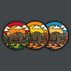 Puede incluir: Tres parches bordados con un bisonte marrón caminando por un paisaje con una puesta de sol de fondo. Los parches son circulares y tienen fondos de diferentes colores: naranja, amarillo y azul.