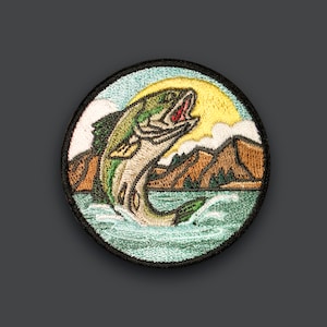 Puede incluir: Parche bordado con un pez verde y marrón saltando fuera del agua con un sol amarillo y montañas en el fondo.