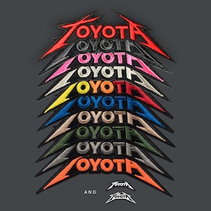 May include: A collection of embroidered patches featuring the word TOYOTA in a stylized, sharp-edged font. The patches are stacked vertically in various colors including red, black, pink, white, yellow, blue, tan, green, grey, and orange.