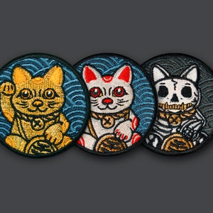 Puede incluir: Tres parches bordados con diferentes estilos de gatos de la suerte. El primer parche presenta un gato dorado con una pata levantada, el segundo parche presenta un gato blanco con acentos rojos, y el tercer parche presenta un gato blanco y negro con una calavera.