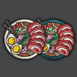 Peut inclure: Deux patchs brodés représentant des bols de ramen avec de la viande rose et blanche, des nouilles, des œufs et des légumes verts.