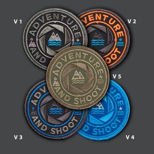 May include: Five embroidered patches with the words "ADVENTURE AND SHOOT" around a camera aperture design with mountains and water. The patches are in black, orange, blue, gray, and olive green.