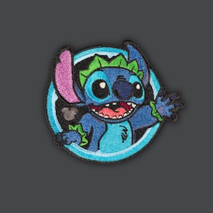 Könnte beinhalten: Blauer, grüner und lilafarbener gestickter Aufnäher von Stitch aus Lilo & Stitch, mit einem blauen Kreis um ihn herum und einer Mickey-Maus-Silhouette im Hintergrund.
