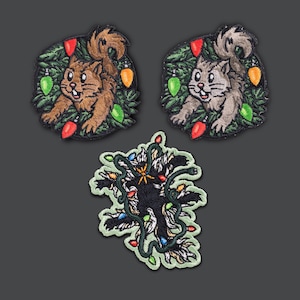 May include: Three embroidered patches featuring a Christmas theme. Two patches depict squirrels surrounded by a wreath of green leaves and colorful Christmas lights. The third patch shows a black creature tangled in Christmas lights.