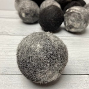 May include: A close-up of a gray and black wool dryer ball. The ball is made of felted wool and has a fuzzy texture.
