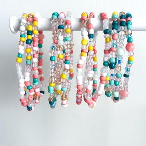 May include: A set of colorful beaded bracelets in shades of pink, teal, yellow, and white. The bracelets are strung on a white background.
