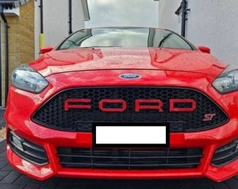 Op de afbeelding: Felrode Ford Focus ST auto. De voorkant toont een zwarte grille met rode "FORD" letters. De auto heeft een strak ontwerp met koplampen en een zwart gebied voor de nummerplaat.