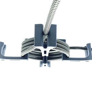 May include: A dark gray, T-shaped object with a coiled, black and white patterned rope. The rope is held in place by the object's design. The background is white.