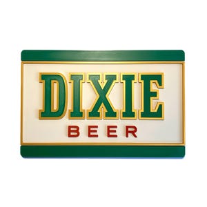 Pode incluir: Uma placa retangular com as palavras "DIXIE BEER" em letras douradas e vermelhas. A placa tem um fundo branco com uma borda verde e detalhes dourados. A placa é provavelmente para um bar ou restaurante.