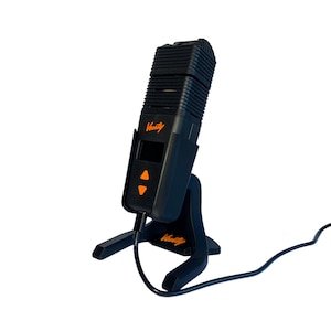 May include: Black vaporizer with the word "Verity" in orange. The device has an orange control panel with up and down arrows. It is mounted on a black stand and has a black power cord.