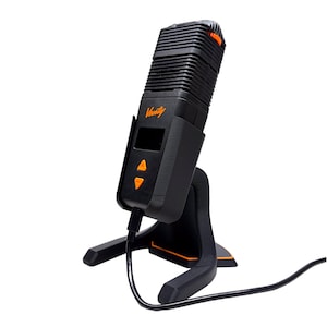 May include: Black and orange vaporizer with the word "Venty" printed on the front. The device has a rectangular shape with a ridged top and sits on a black stand. It features a small screen and two orange buttons.