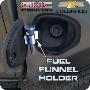 May include: A white ceramic mug with a black handle and the text "But First, Coffee" in a black, handwritten-style font. The mug is on a white surface.