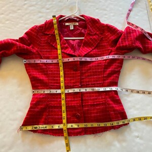 May include: A red and white checkered blazer with a button closure. The blazer is measured with a tape measure, showing the length of the blazer is 18 inches, the bust is 16 inches, and the waist is 14 inches.