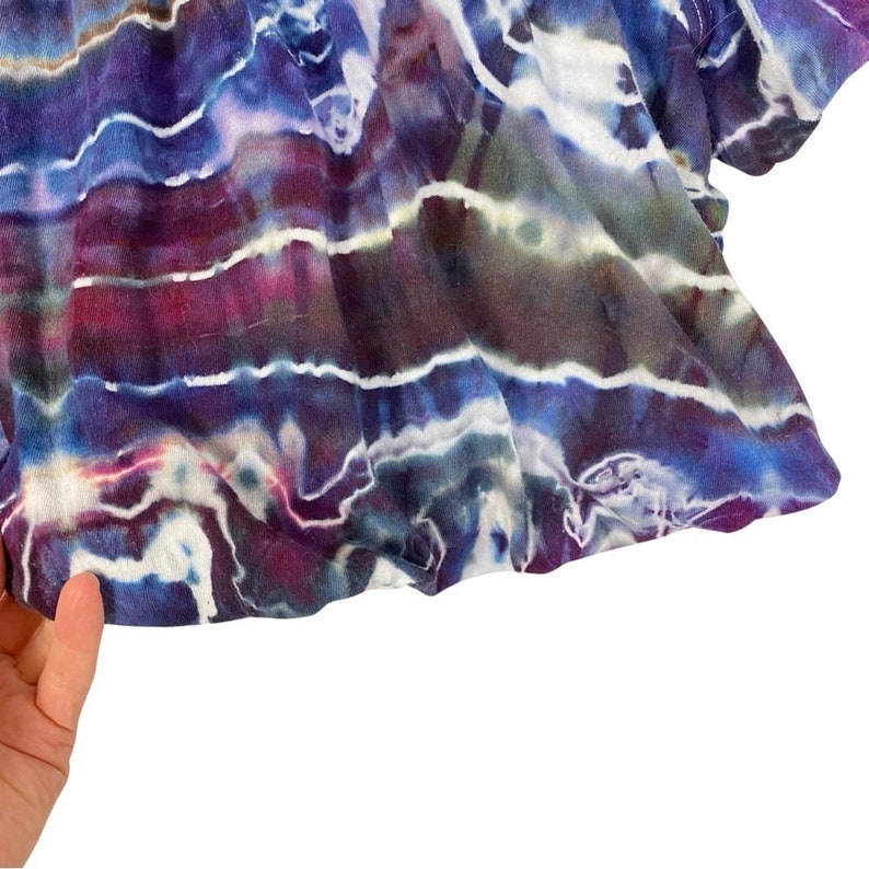 May include: A tie-dye fabric with a blue, purple, and white color scheme. The fabric has a striped pattern with a wavy, abstract design.