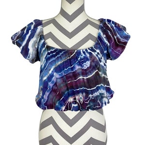 May include: A blue and purple tie-dye crop top with short, puffed sleeves and a square neckline.