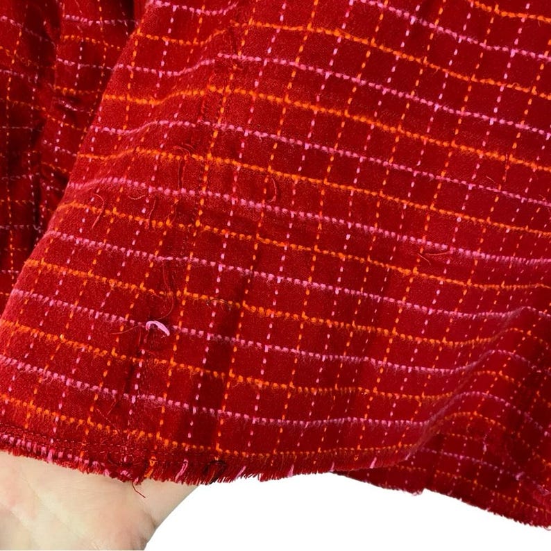 May include: Red fabric with a pink and orange grid pattern. The fabric has a frayed edge.