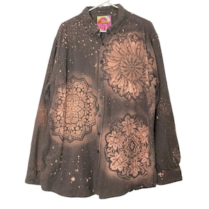 May include: A long-sleeved button-down shirt with a brown and white checkered pattern. The shirt features large, intricate floral designs in a lighter brown color. The collar has a colorful tag that says "Heaven".