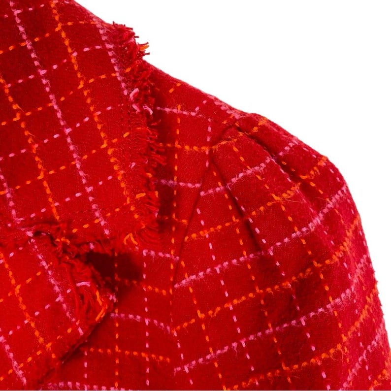 May include: Red and pink plaid fabric with a fringed edge. The fabric has a woven texture.