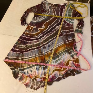May include: A long-sleeved, tie-dye dress with a loose fit and a round neckline. The dress is made of a soft, flowing fabric and features a colorful swirl pattern in shades of brown, blue, white, and yellow.