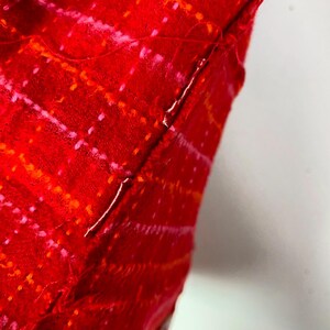 May include: Close-up of a red fabric with a pink and orange pattern. The fabric is sewn together with a white thread.