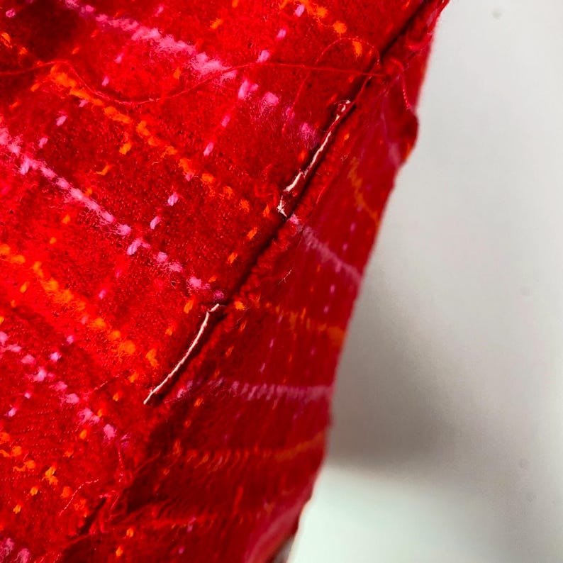 May include: Close-up of a red fabric with a pink and orange pattern. The fabric is sewn together with a white thread.