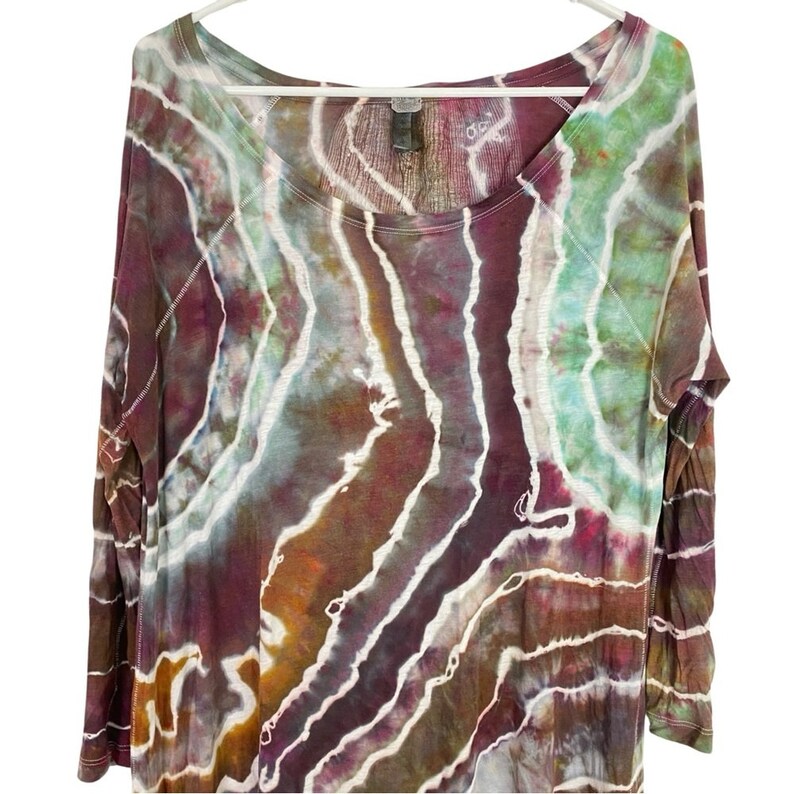 May include: A long-sleeved, tie-dye shirt with a scoop neck. The shirt features a swirling pattern of purple, green, brown, and white.