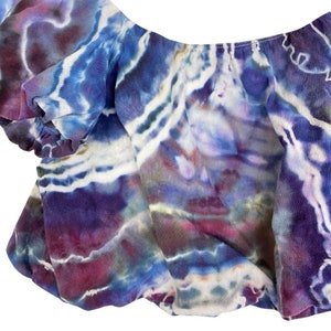 May include: A purple, blue, and white tie-dye off-the-shoulder top with a ruffled neckline.