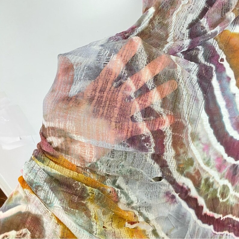 May include: A sheer, lightweight fabric with a tie-dye pattern in shades of purple, orange, and yellow. The fabric has a textured, woven appearance.