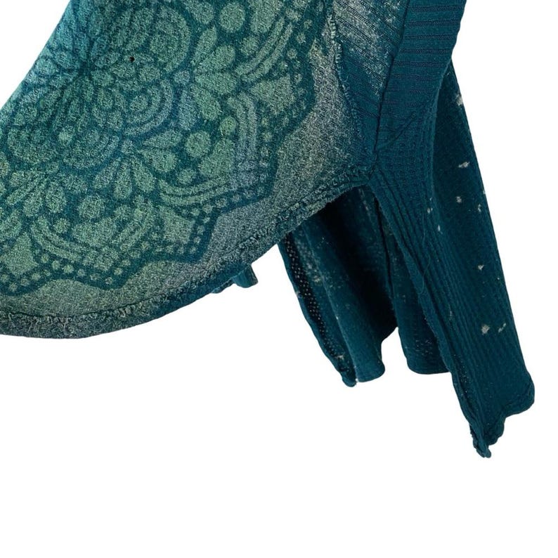 May include: Teal blue waffle knit sweater with a faded mandala design. The sweater has a relaxed fit and a slightly cropped length.